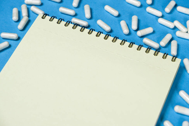 Medical notepad with pills on a blue background, space for text. - Foto, afbeelding