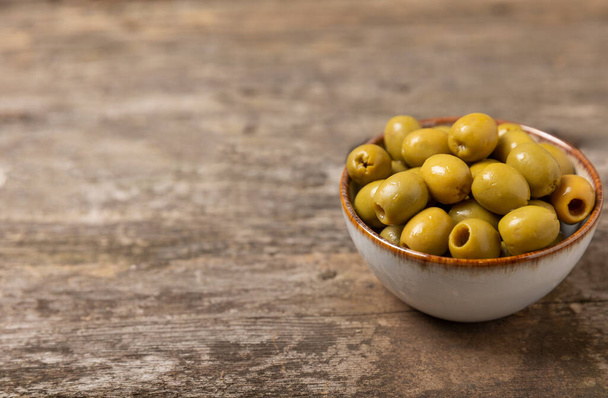 Green olives with leaves in bowls on a textured old wood background. Delicious and healthy food. Delicacy.Mediterranean Kitchen. Place for text. copyspace. - Photo, Image