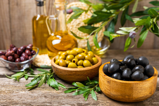 Zöld, fekete és piros olívabogyó levelekkel tálakban, textúrázott, régi fa háttéren. Finom és egészséges ételek. Csemege. Mediterrán konyha. Helyet az sms-nek. másolótér. - Fotó, kép