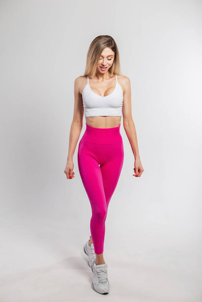 Beautiful happy sporty stylish fitness woman with slender body in sportswear with sneakers walks on a white background. - Valokuva, kuva