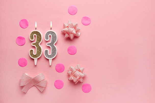 Número 33 sobre fondo rosa pastel con decoración festiva. Feliz cumpleaños velas. El concepto de celebrar un cumpleaños, aniversario, fecha importante, vacaciones. Copiar espacio. Banner - Foto, imagen
