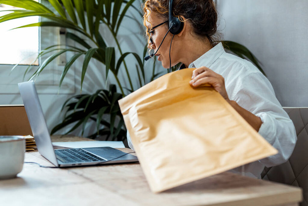Call center service customer care clients satisfaction and tracking package online office concept image. Woman working wearing headset and using laptop with big letter package and computer. Busy lady - Φωτογραφία, εικόνα