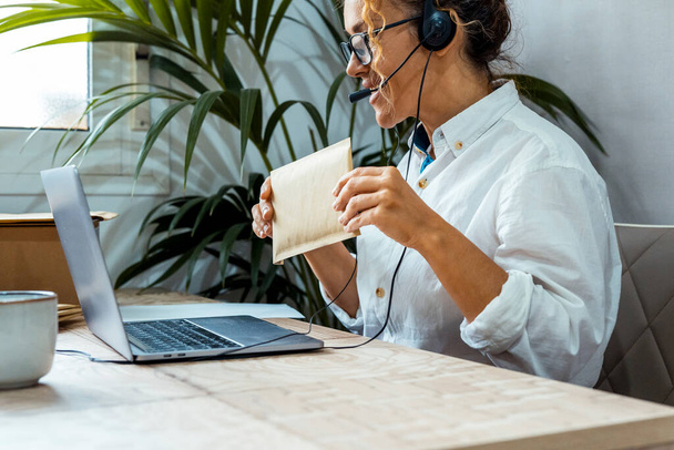 Happy professional worker talking online in video call conference using headset and microphone. Concept of customer care service call center. One busy job woman worker showing letter at the screen - Photo, Image