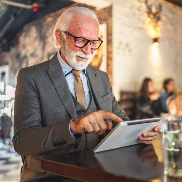 Ein Senior Mann kaukasischen männlichen Geschäftsmann Geschäftsinhaber verwenden digitales Tablet sitzen im Café tragen Anzug Kopierraum - Foto, Bild