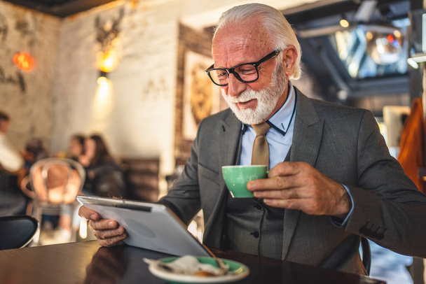 Один старший чоловік кавказький бізнесмен власник використовує цифровий планшет сидить у костюмі кав'ярні костюм костюм простір має чашку кави
 - Фото, зображення