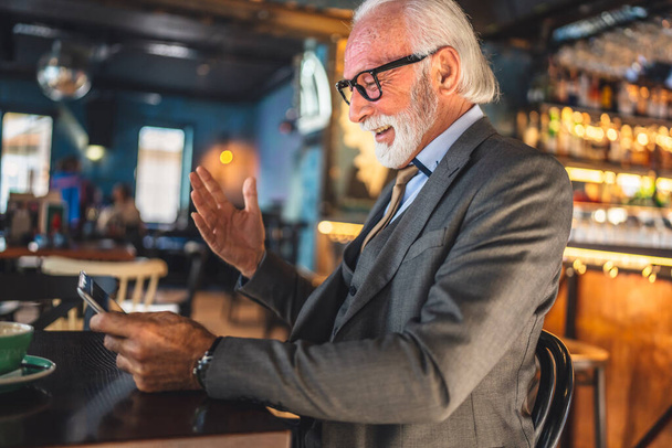 Egy idős férfi kaukázusi férfi üzletember üzletember tulajdonos használja digitális tabletta ül a kávézóban van videó hívás beszélgetés kapcsolat és kommunikációs viselet ruha másolás hely - Fotó, kép