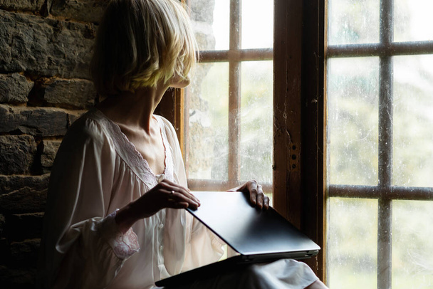 A woman closes a laptop near the window. End of work. Freelancer, work from home. - 写真・画像