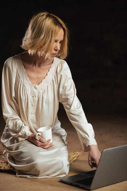 Woman with coffee and laptop. Workaholism, deadline concept. Dark background. Empty room. - Foto, Bild