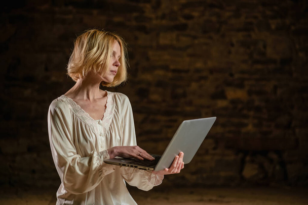 Woman and laptop in an empty dark room. Deadline, a lot of work, privacy. Middle age woman in a white shirt. - Foto, Imagen