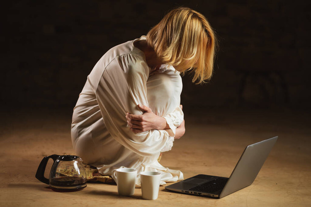 Woman with coffee cup in front of laptop. Empty room, dark background. Deadline, recycling, hard work freelancer concept. - Foto, Imagen