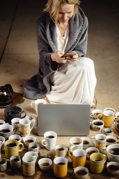 A woman with a phone in her hands in front of a laptop and many cups of coffee. Deadline, recycling concept. - Foto, Imagen