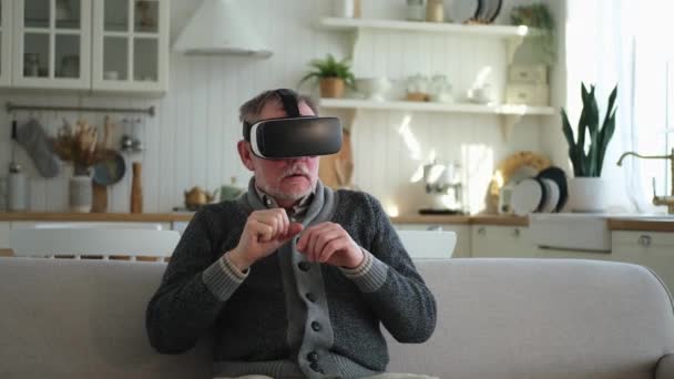 Emocionado hombre mayor maduro usando gafas de realidad virtual metaverse VR auriculares en casa. Abuelo tocando el aire durante la experiencia VR en casco de realidad virtual. Videojuego de simulación de alta tecnología - Imágenes, Vídeo