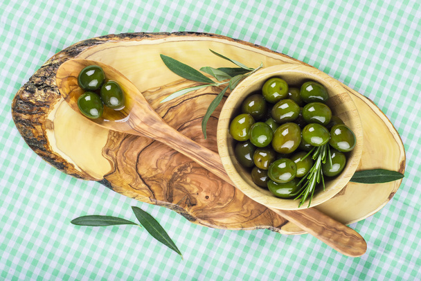 Ciotola di legno e cucchiaio con olive verdi e olio d'oliva
 - Foto, immagini