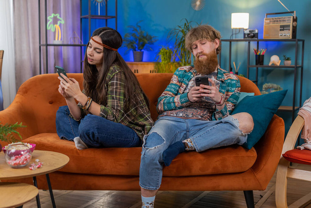 Családi házasság hippi pár férfi nő használ okostelefonok vita után veszekedés. Férj és feleség együtt semmibe veszik egymást a kanapén a szobában. Kommunikációs problémák, közösségi média hálózati függőség - Fotó, kép