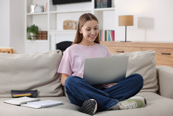 Онлайн обучение. Девочка-подросток с ноутбуком на диване дома - Фото, изображение