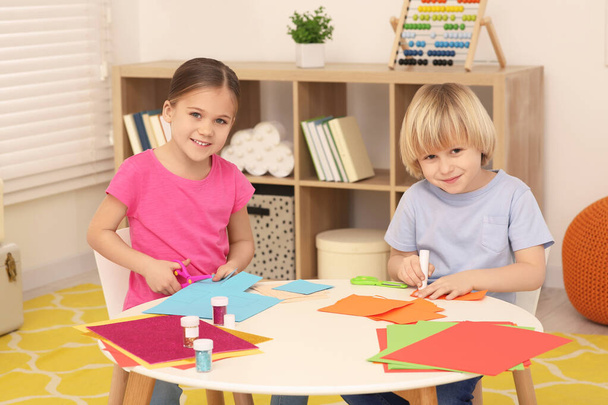 Girl cutting colorful paper and boy using glue stick at desk in room. Home workplace - Foto, imagen