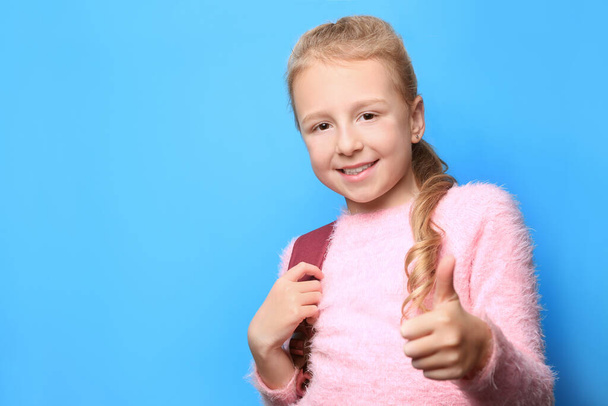 Happy little girl with backpack showing thumbs up on light blue background. Space for text - Foto, immagini