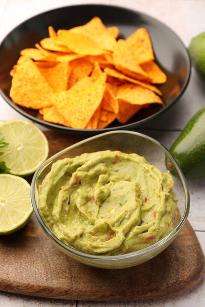 Bol de délicieux guacamole servi avec des chips de nachos et du citron vert sur une table blanche - Photo, image