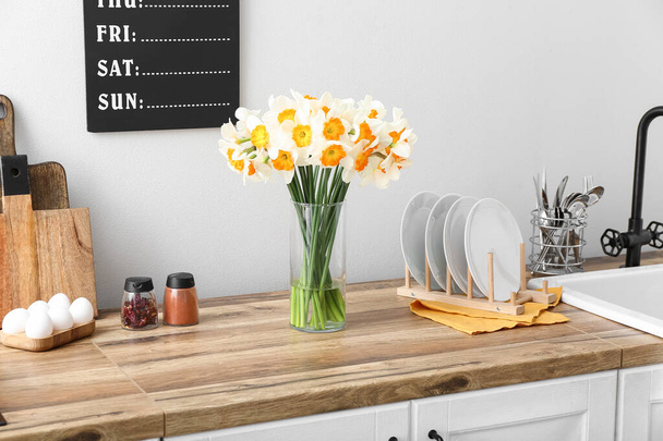 Vase with blooming narcissus flowers on wooden counter in interior of modern kitchen - 写真・画像