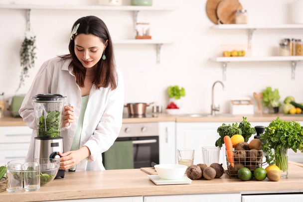 Mujer joven haciendo jugo de verduras con licuadora en la cocina - Foto, Imagen