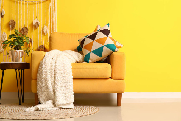 Уютное кресло с клетчатой и кожаной обивкой на кофейном столике возле желтой стены - Фото, изображение