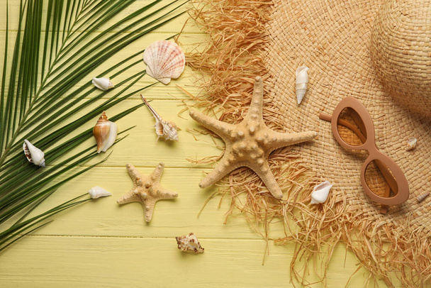 Összetétel stílusos kalap, napszemüveg, tengeri csillagok, kagylók és pálmalevél színes fa háttér - Fotó, kép