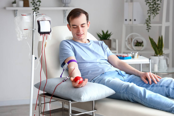 Young man with grip ball donating blood in clinic - Foto, Bild