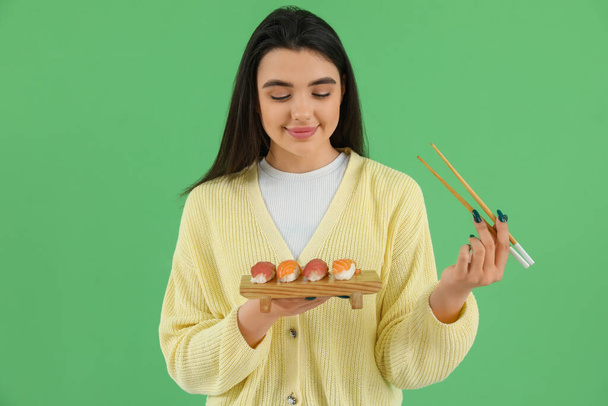 Happy young woman with sushi and chopsticks on green background - Photo, Image
