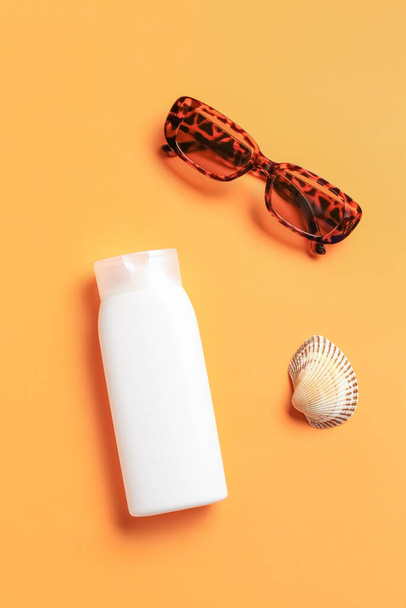 Bottle of sunscreen cream with sunglasses and seashell on orange background - Фото, изображение