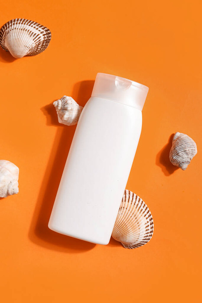 Бутылка крема от загара с ракушками на оранжевом фоне - Фото, изображение