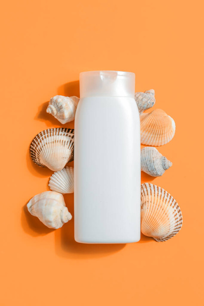 Bottle of sunscreen cream with seashells on orange background - Foto, Imagen