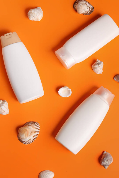 Бутылки крема от загара с ракушками на оранжевом фоне - Фото, изображение