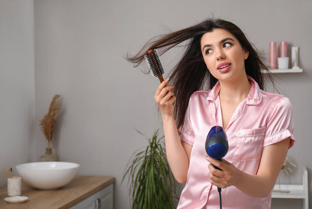 Pretty young woman with hair dryer and brush in bathroom - Foto, Imagem