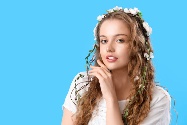 青い背景に彼女の髪に花を持つ美しい若い女性。夏至 - 写真・画像