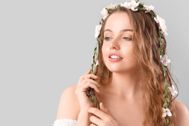 Beautiful young woman with flowers in her hair on light background. Summer solstice - Fotoğraf, Görsel