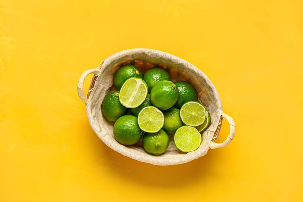 Basket with fresh limes on yellow background - Photo, Image