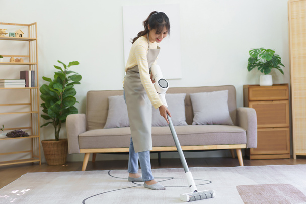 Maagd met behulp van draadloze stofzuiger te stofzuigen en het reinigen van het stof op het tapijt in huis. - Foto, afbeelding