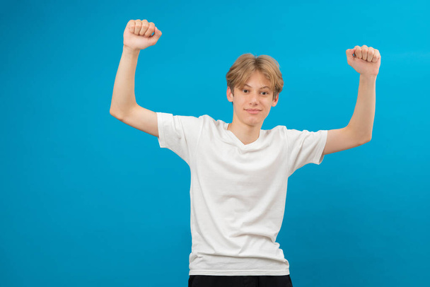 Extremely excited overjoyed teen boy shouting making yes gesture, amazed with his victory, triumph. Indoor studio shot isolated on blue background - Photo, Image