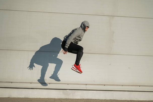 Caucasian man in hoodie jumping high with hands on knees outdoors - Photo, Image