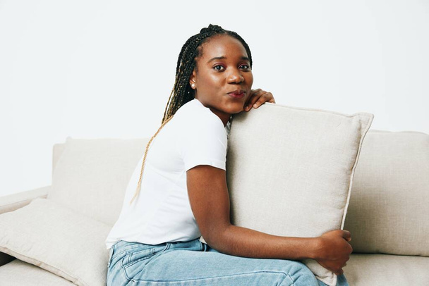Onnellinen afrikkalainen amerikkalainen nainen istuu kotona sohvalla, lepää ja loma hymy, kevyt tausta. Rentoutunut kotielämä, vapaapäivä. Laadukas kuva - Valokuva, kuva