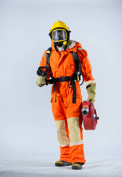 Profesionální hasič stojící sebevědomě na bílém pozadí při držení požární hadice. - Fotografie, Obrázek