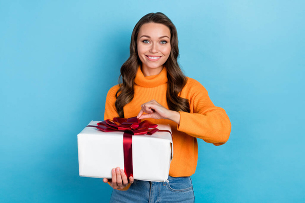 Photo of pretty charming woman dressed orange sweater smiling gift box isolated blue color background. - Fotó, kép