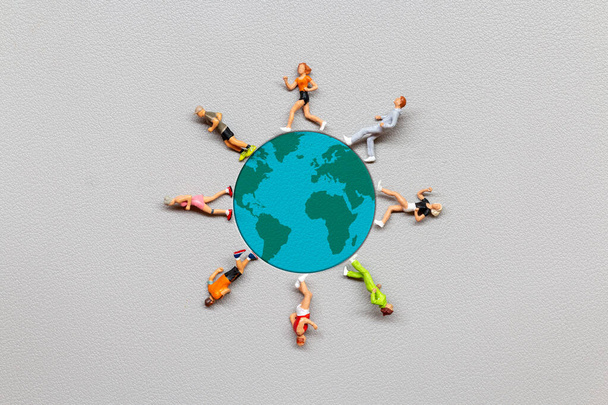 Miniaturmenschen auf der Erdkugel mit grauem Hintergrund, Konzept zum Weltbevölkerungstag - Foto, Bild