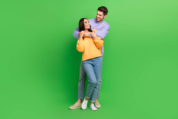 Full size photo of two cheerful lovely partners cuddle look each other isolated on green color background. - Foto, Imagen