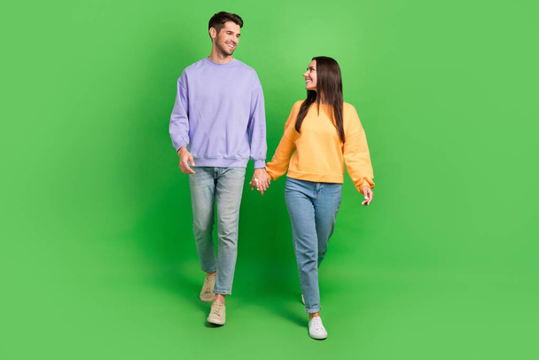 Full body portrait of two lovely peaceful partners hold hands walking look each other isolated on green color background. - Valokuva, kuva