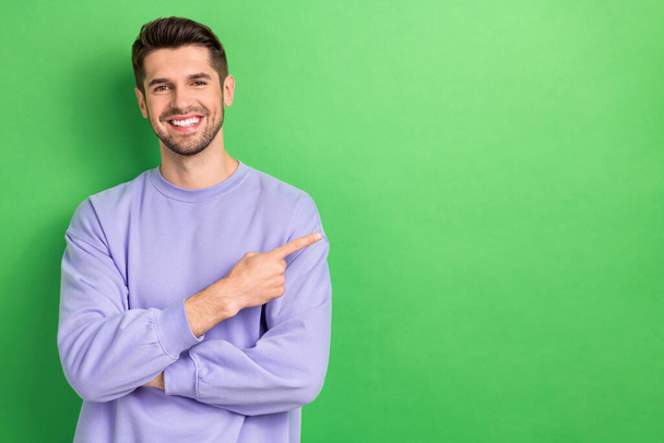 Photo of confident charming young man wear purple smiling pointing finger empty space isolated green color background. - Valokuva, kuva