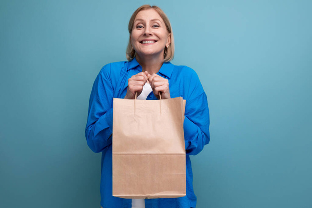 happy middle aged woman holding craft eco friendly bag on blue copy space background. - Photo, Image