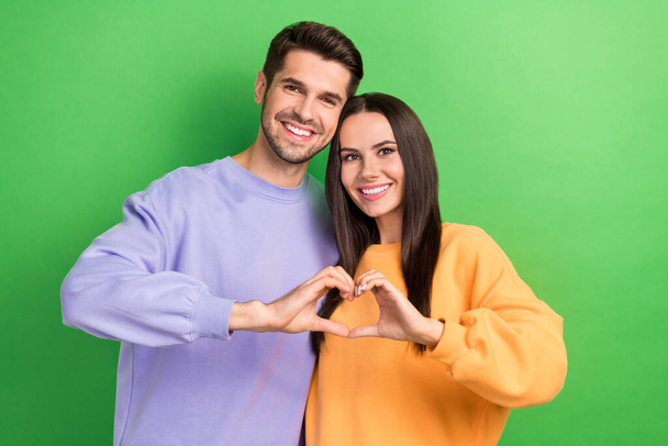 Photo of pretty adorable boyfriend girlfriend wear sweatshirts showing arms heart cuddling isolated green color background. - Zdjęcie, obraz