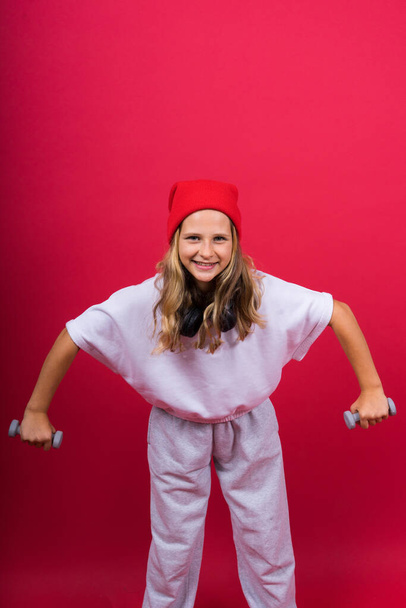 Kid girl doing fitness exercises with dumbbells on a red background - Foto, Imagem
