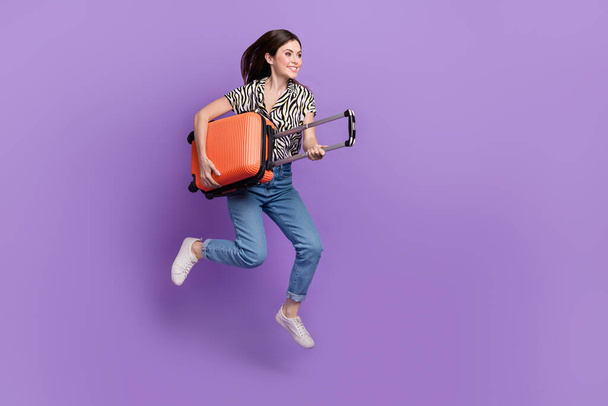 Full size profile photo of cheerful pretty girl jumping hold suitcase empty space isolated on violet color background. - Foto, Imagen